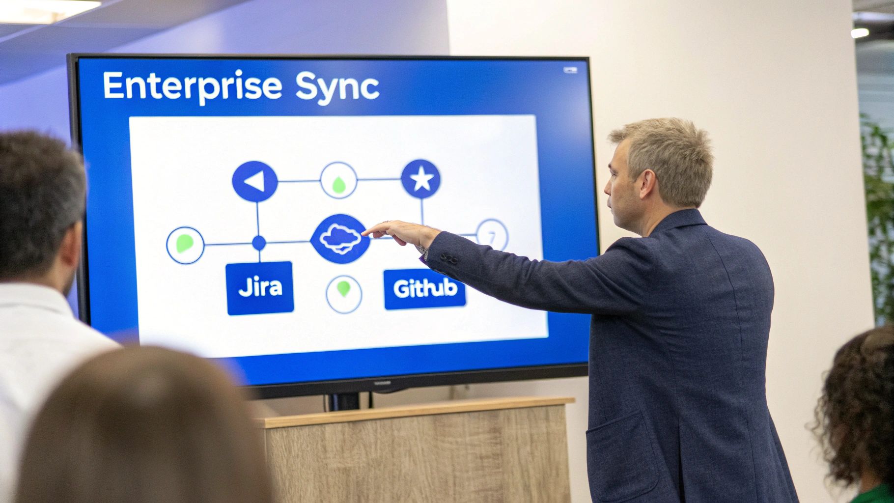 A man in a suit presents a diagram showing Enterprise Sync, Jira, and Github connections.